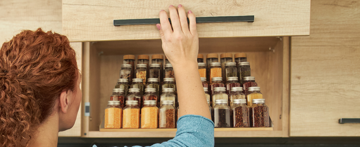 A woman uses a seasoning jar from a spice rack in kitchen cabinet